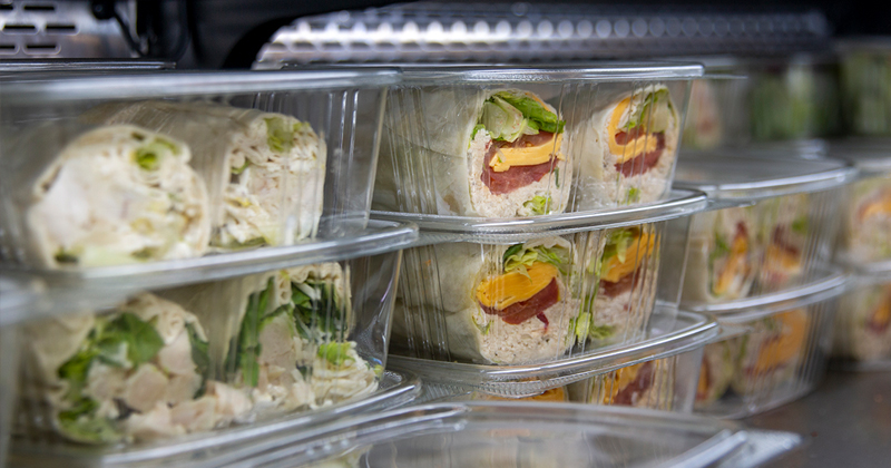 Clear plastic containers holding halved wraps with visible fillings in a commercial food service display