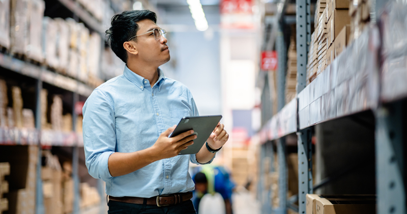 Warehouse staff using a tablet to check the stock inventory on shelves